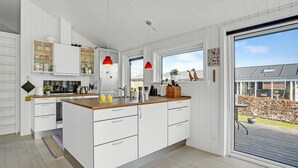 A modern kitchen with white cabinetry, a wooden countertop, and a large island. There are two pendant lights, a refrigerator, and a window with a view of the outside. - Beautiful home in Juelsminde with WiFi (Horsens)