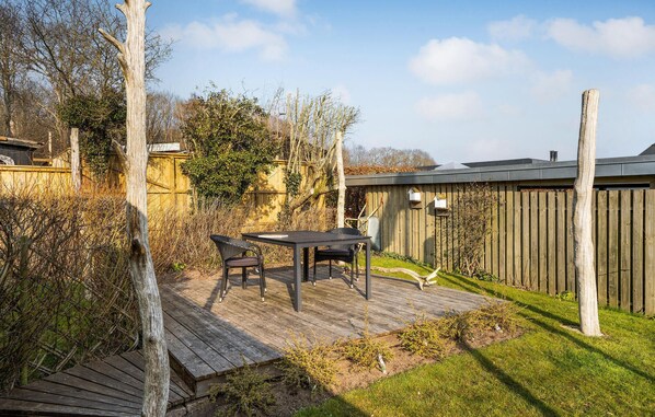 A wooden deck with a table and chairs, surrounded by a wooden fence and trees.