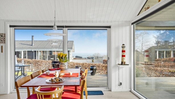 A dining area with a table set for four, a potted plant, and a view of a modern house and garden through large windows. - Beautiful home in Juelsminde with WiFi (Horsens)