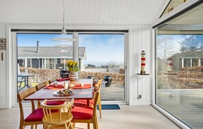 A dining area with a table set for four, a potted plant, and a view of a modern house and garden through large windows.