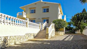 A two-story building with a stone staircase leading to the entrance, surrounded by a white fence and greenery. - Beautiful home in La Font den Carros (La Font den Carros)