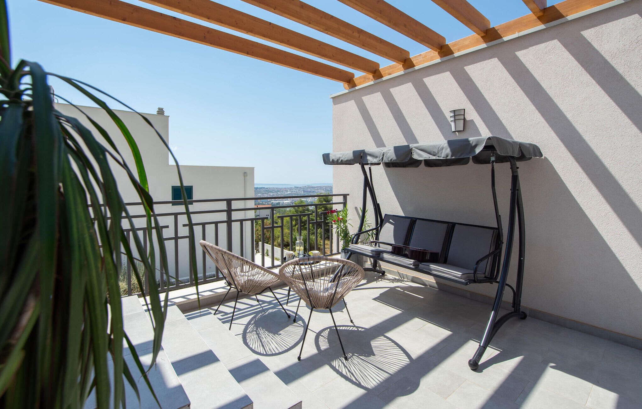 En balkon med gyngestol, et bord og en sofa under et pergola