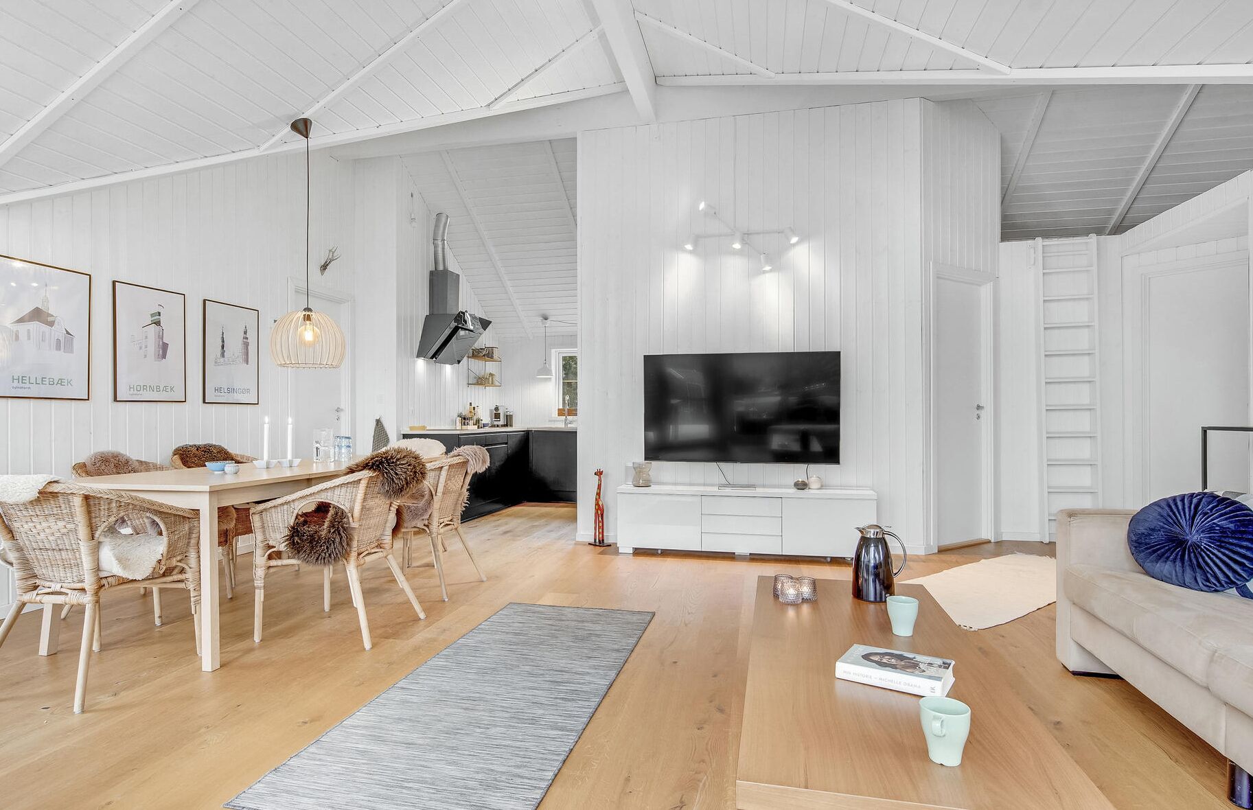 A spacious living room with a large TV, wooden flooring, and a dining area with wicker chairs.