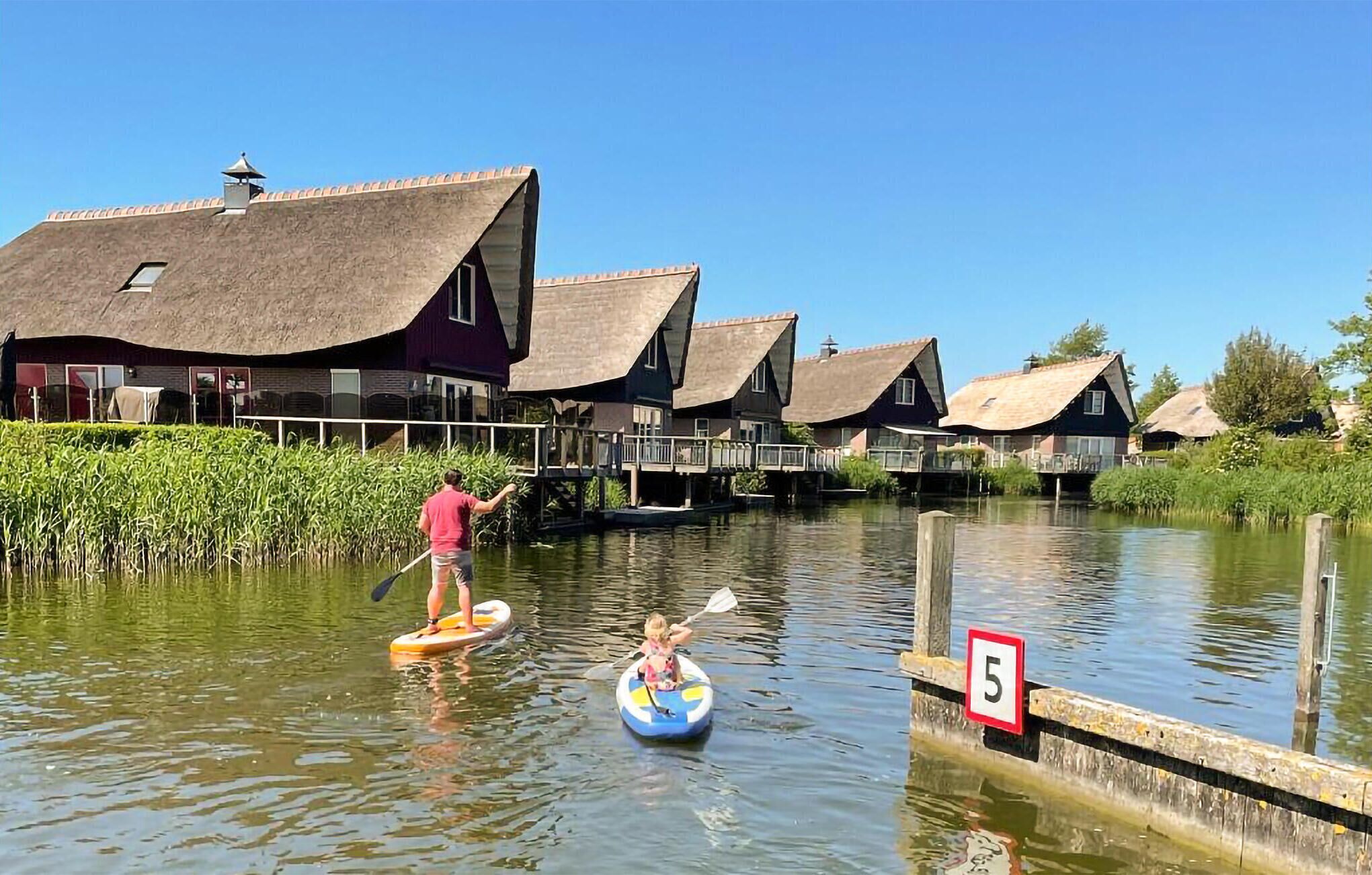 A canal with houses on stilts, a person paddling a boat, and a speed limit sign.