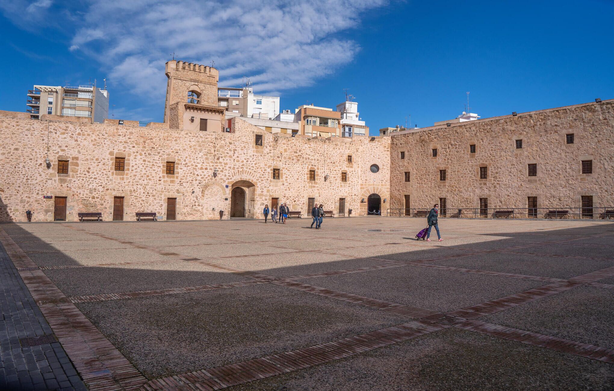 A courtyard with stone buildings, a central archway, and a tower.