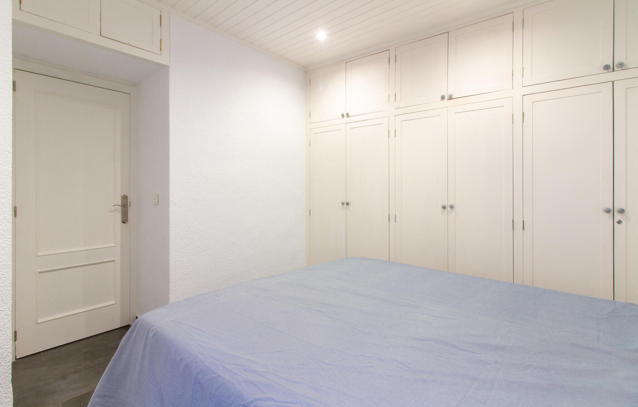 Un dormitorio con una cama individual, paredes blancas y un armario grande con múltiples puertas.