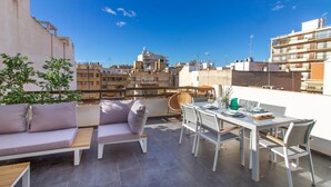 Una terraza en la azotea con una mesa de comedor para cuatro personas, un sofá y una silla.