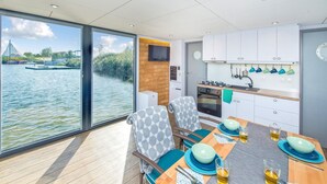 Een moderne keuken met uitzicht op een rivier, een eethoek met blauw en groen servies, en een groot raam met uitzicht op het water.