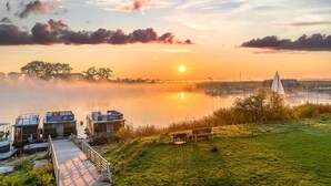 Uitzicht op een meer met een houten steiger, een gazon met een bankje en een klein gebouw met borden.