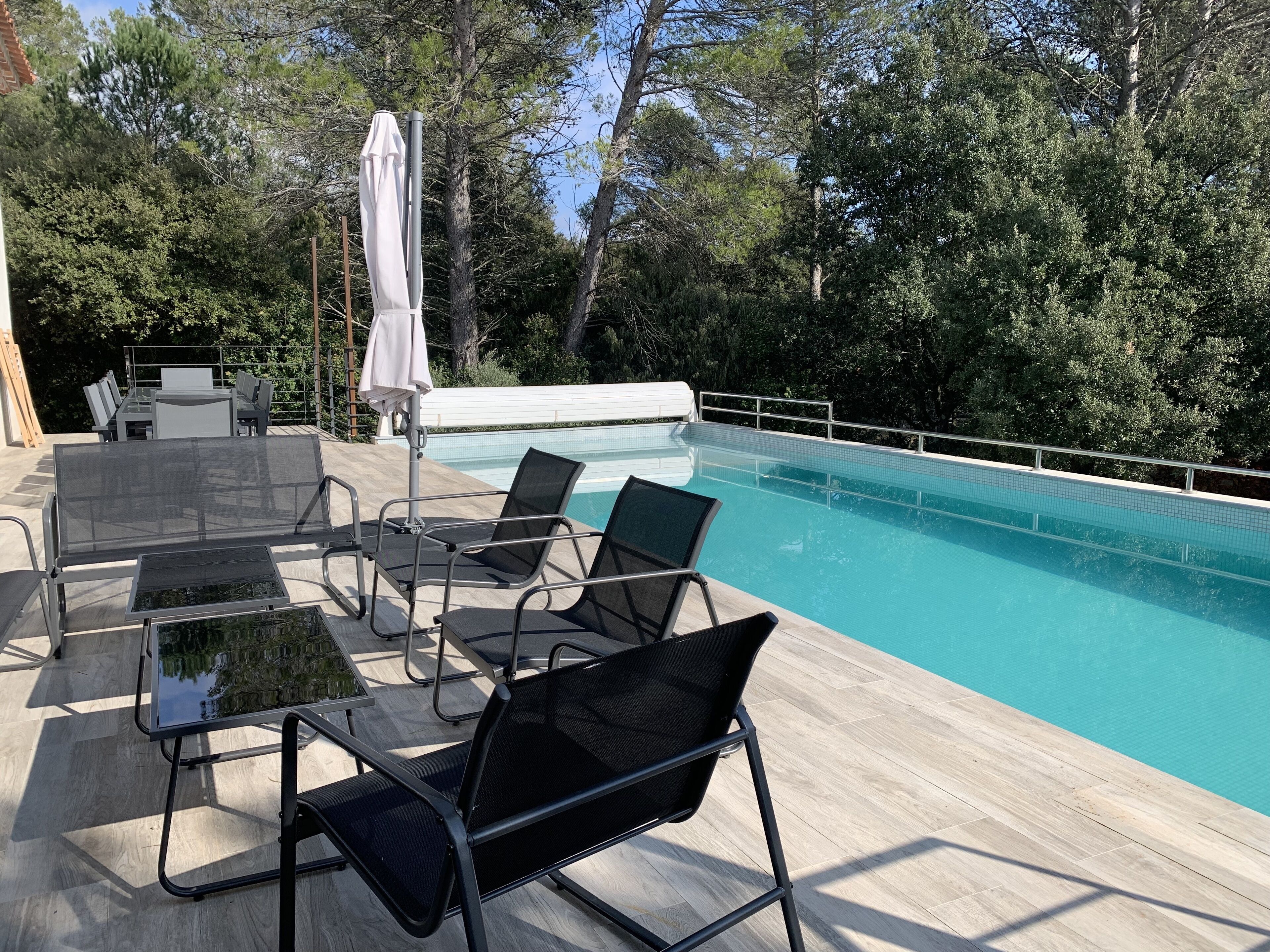 An outdoor pool area with a wooden deck, lounge chairs, and a table with chairs.
