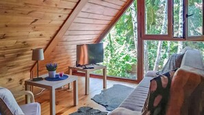 Ein gemütliches Dachzimmer mit schrägverlaufender Holzwand, einem Fernseher auf einem kleinen Tisch, einer Couch und Blick ins Grüne.