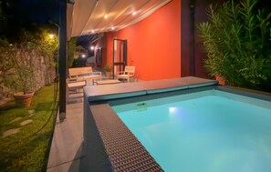 A swimming pool with a sunken seating area, a stone wall, and a potted plant.