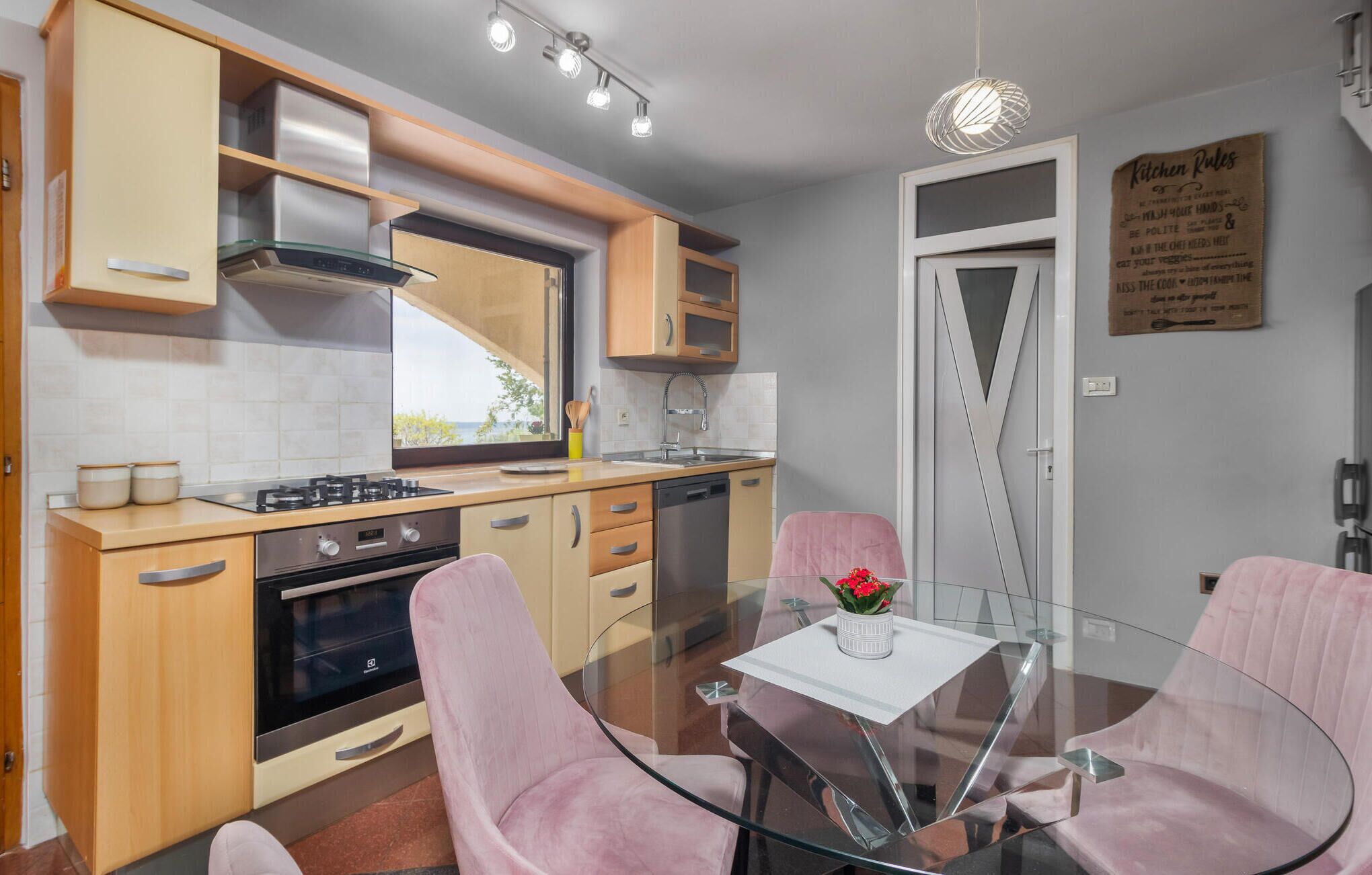 Une cuisine moderne avec une table à manger en verre, des chaises roses et une vue sur l’extérieur.