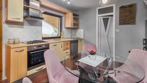 Een moderne keuken met een glazen eettafel, roze stoelen en uitzicht op het buiten.