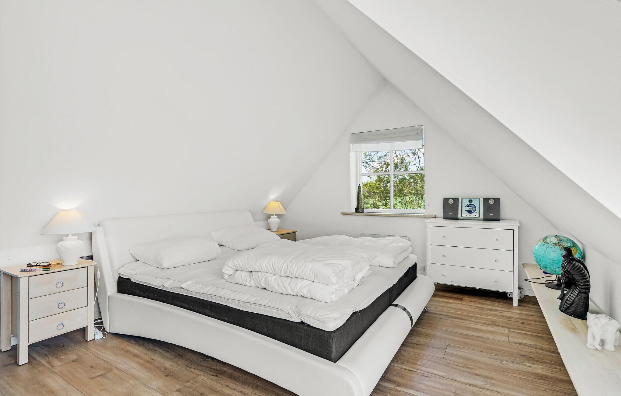 A bedroom with a bed, bedside tables, a window, and a dresser.