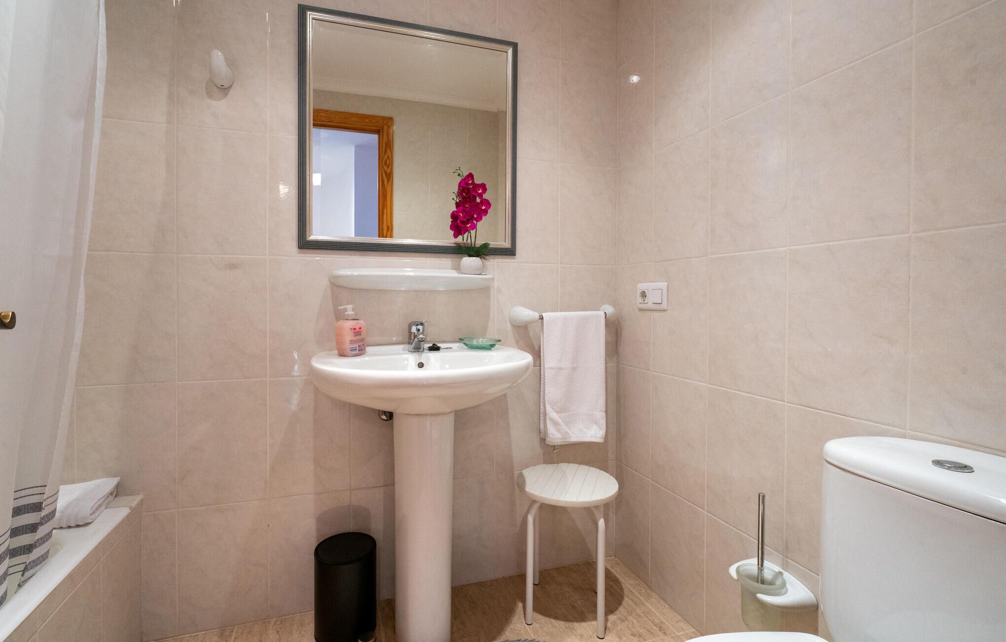 A bathroom with a pedestal sink, a mirror, a toilet, and a small trash bin.