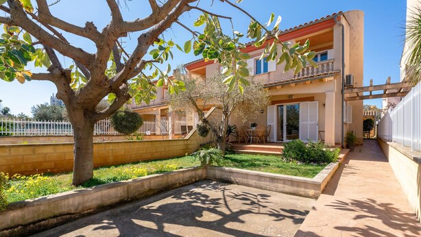 Ein zweistöckiges Haus mit Balkon, ein Garten mit Baum und einem gepflasterten Weg.