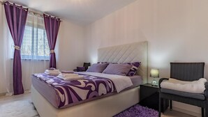 A bedroom with a large bed, a nightstand, a chair, and a window with purple curtains. - 2 bedroom beautiful apartment in Liznjan (Liznjan)