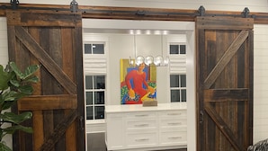Une pièce dotée d’une porte coulissante de style grange, de meubles blancs, d’un tableau coloré et d’une plante en pot.