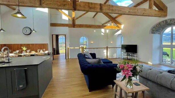 A spacious living area with a wooden ceiling, a sofa, a TV, and a view of the outdoors. - Amazing Chapel near Yr Wyddfa (Snowdon) and Zip World (Llanrug)
