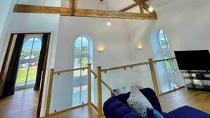 A spacious room with exposed wooden beams, large windows, and a blue sofa. - Amazing Chapel near Yr Wyddfa (Snowdon) and Zip World (Llanrug)