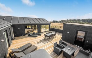 Eine moderne Außenterrasse mit Holzboden und schwarzer Möbel, darunter Lounge-Stühle und ein Esstisch.