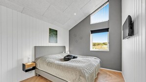 Une chambre à coucher comprenant un lit, une table de chevet, un téléviseur fixé au mur et une fenêtre donnant sur l’extérieur.