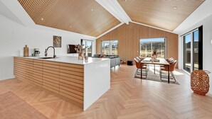 Une cuisine moderne dotée d’un îlot central, d’un plafond avec des lambris en bois et de grandes fenêtres offrant une vue sur l’extérieur.