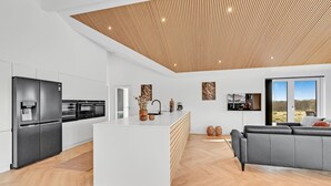 Une cuisine moderne dotée d’un îlot central, d’un coin repas avec un canapé et d’une grande fenêtre offrant une vue dégagée.