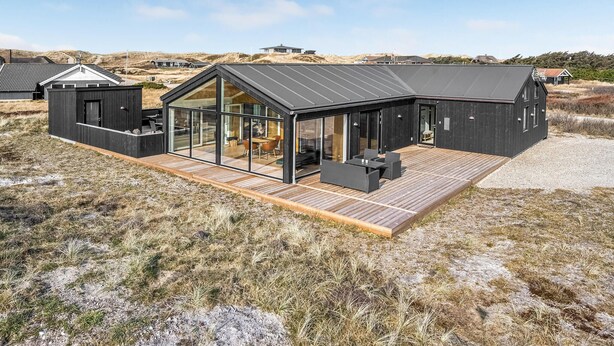 Une maison moderne dotée d’une grande façade vitrée, d’une terrasse en bois et offrant une vue sur le paysage environnant.