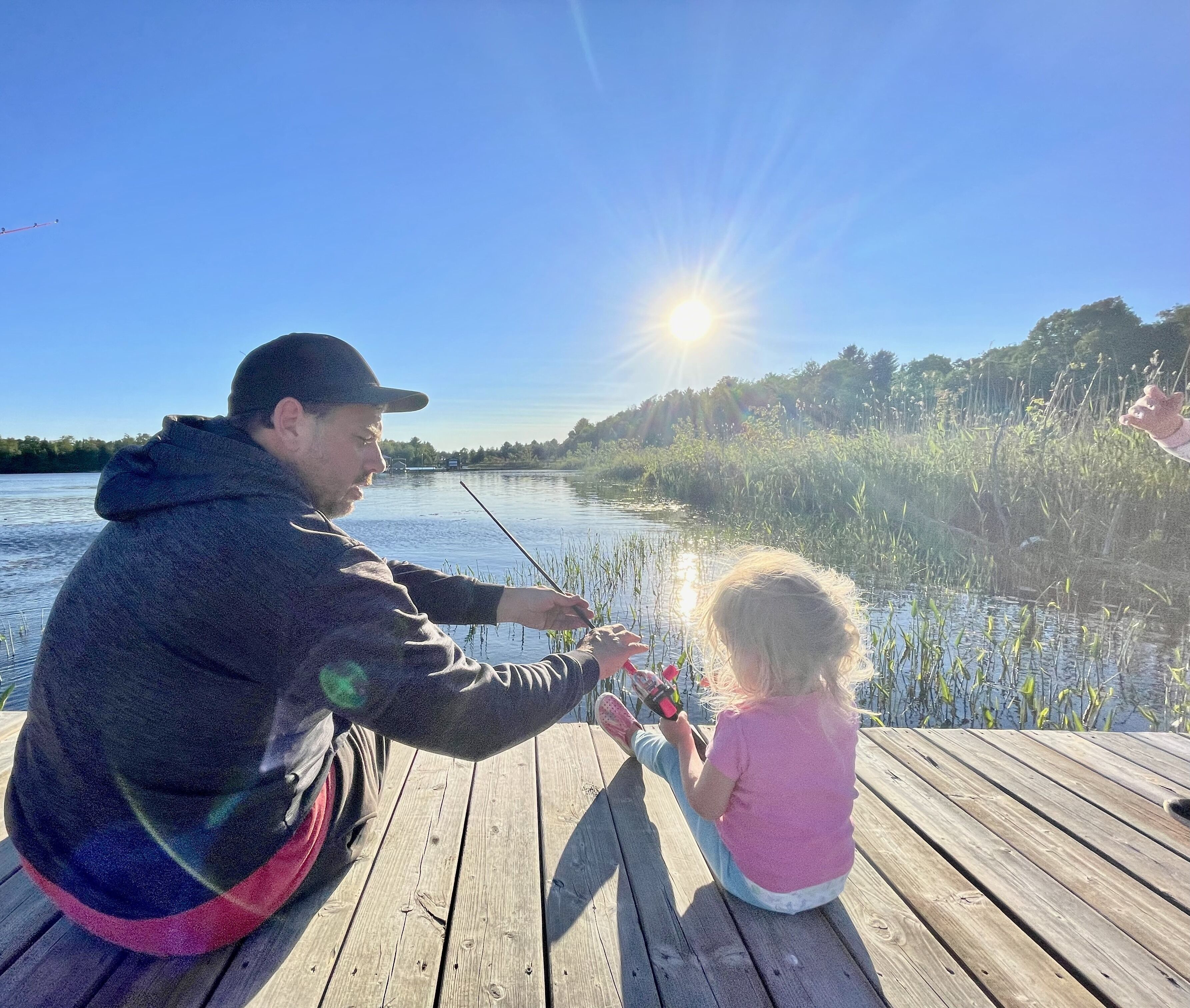 Une jetée en bois au bord d’un lac, où une personne et un enfant pêchent.
