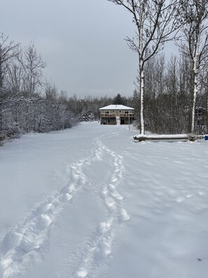 Schneebedeckte Landschaft mit einem zweistöckigen Gebäude, das einen Balkon und eine Garage hat.