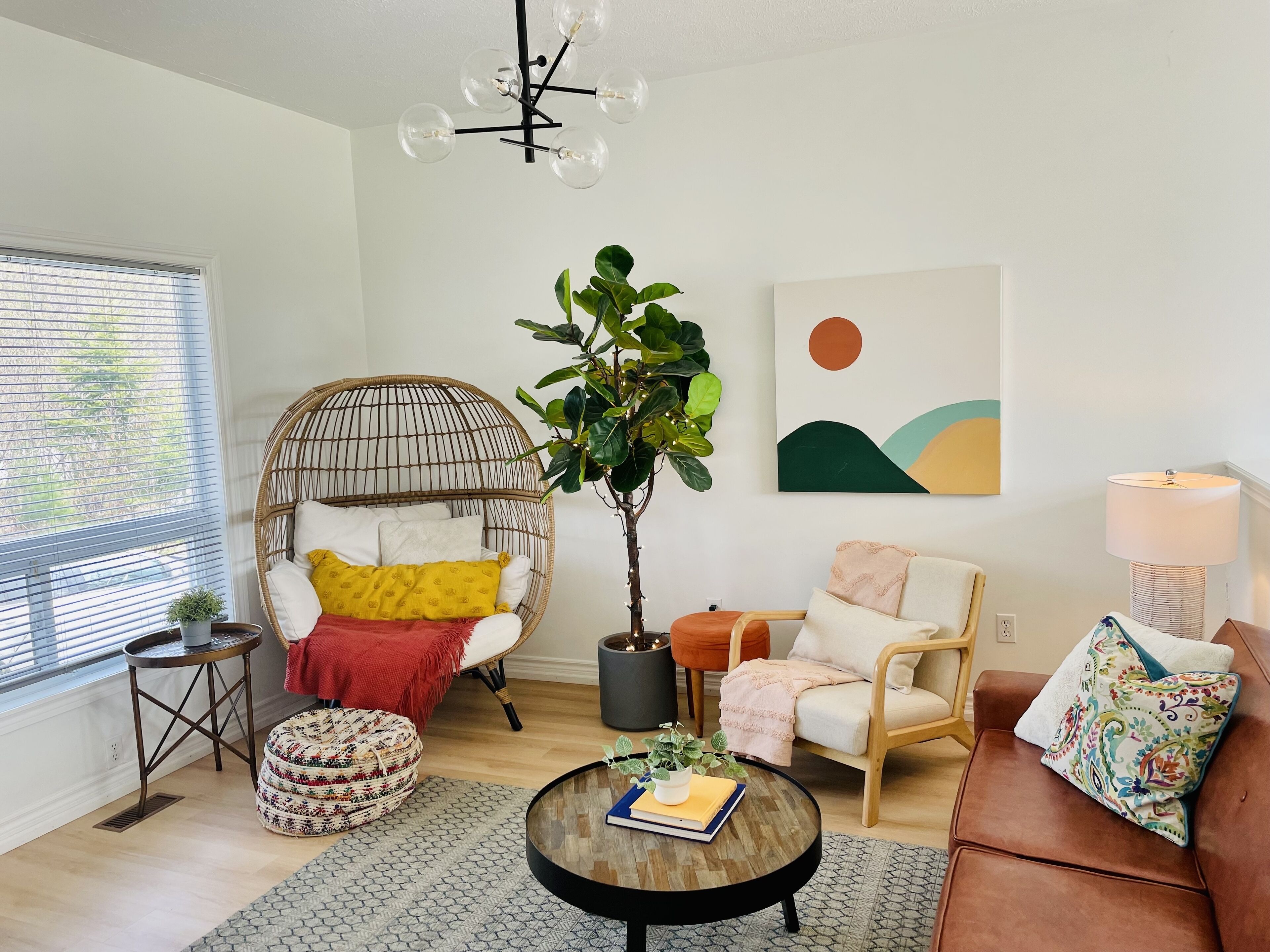 Un salon chaleureux avec un fauteuil en osier, une table basse ronde sur laquelle repose un livre, une plante en pot et un coussin coloré.