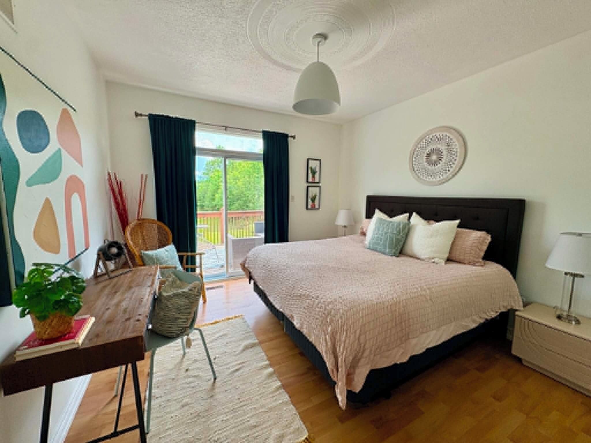 Une chambre à coucher comprenant un lit, un bureau, une chaise, une lampe et une vue sur l’extérieur, visible à travers une porte vitrée.