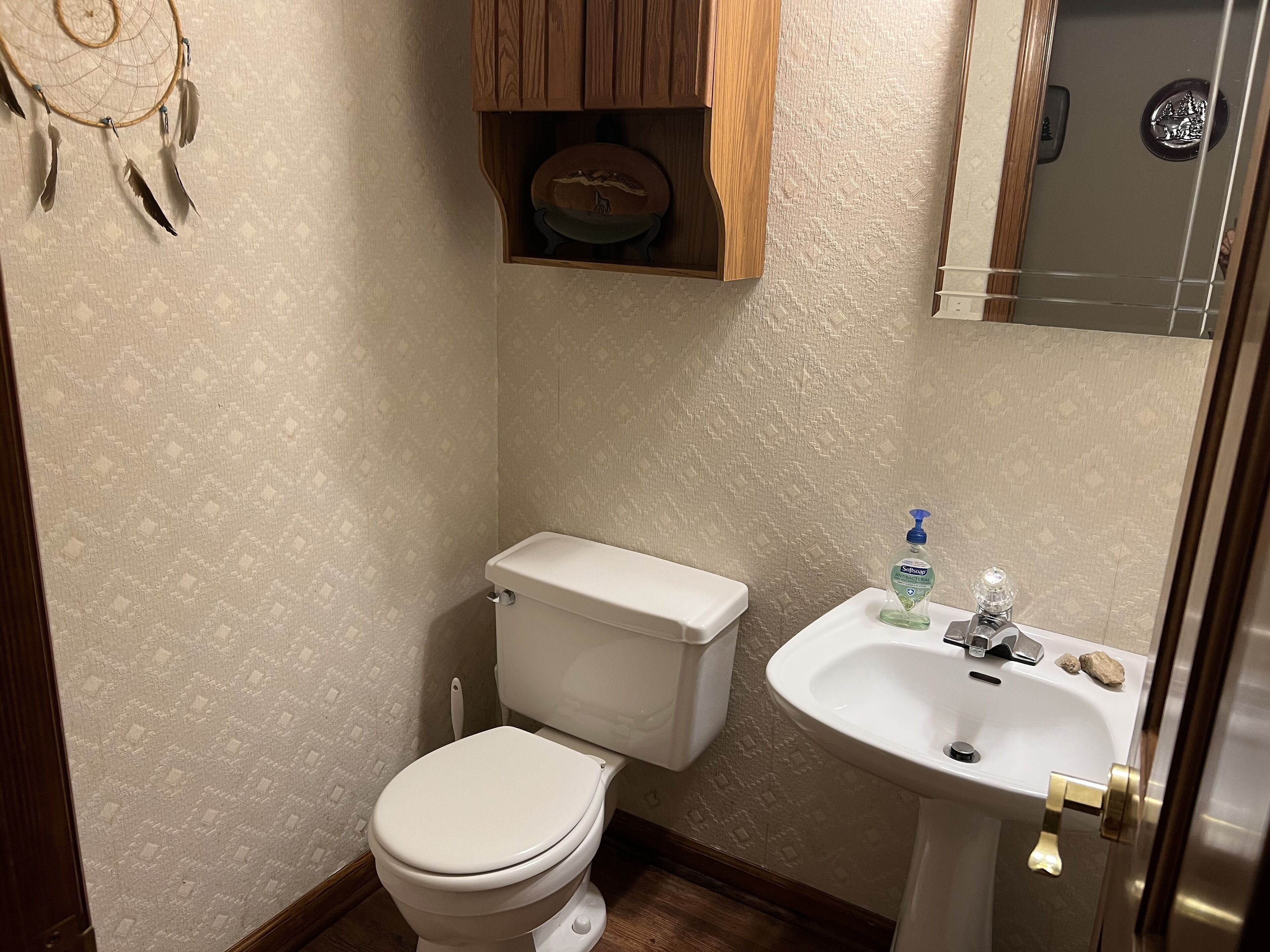 Un baño pequeño con inodoro, lavamanos y un atrapasueños en la pared.