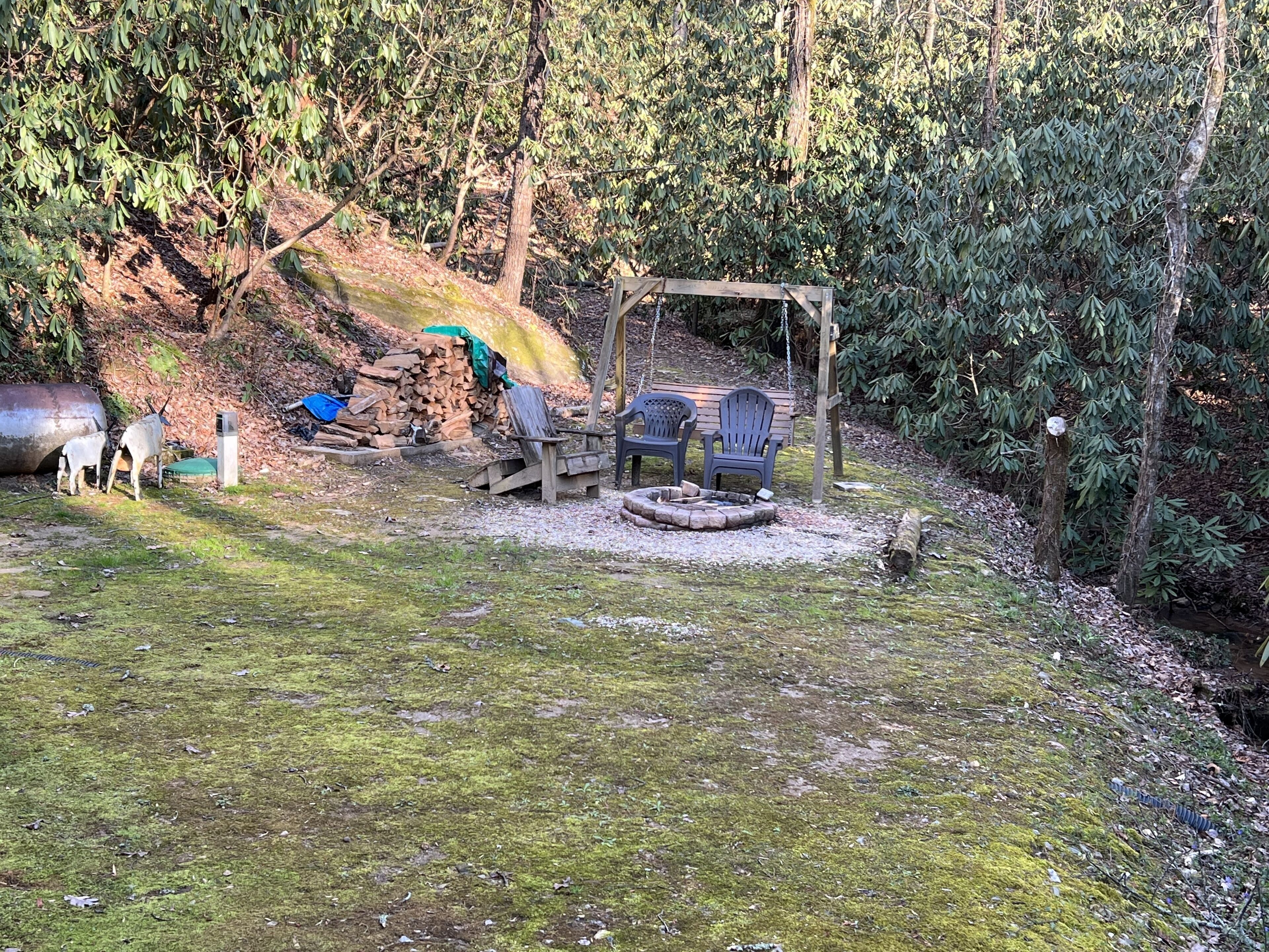 Eine rustikale Outdoor-Umgebung mit Feuerschale, Sitzgelegenheiten und einem Holzstapel.