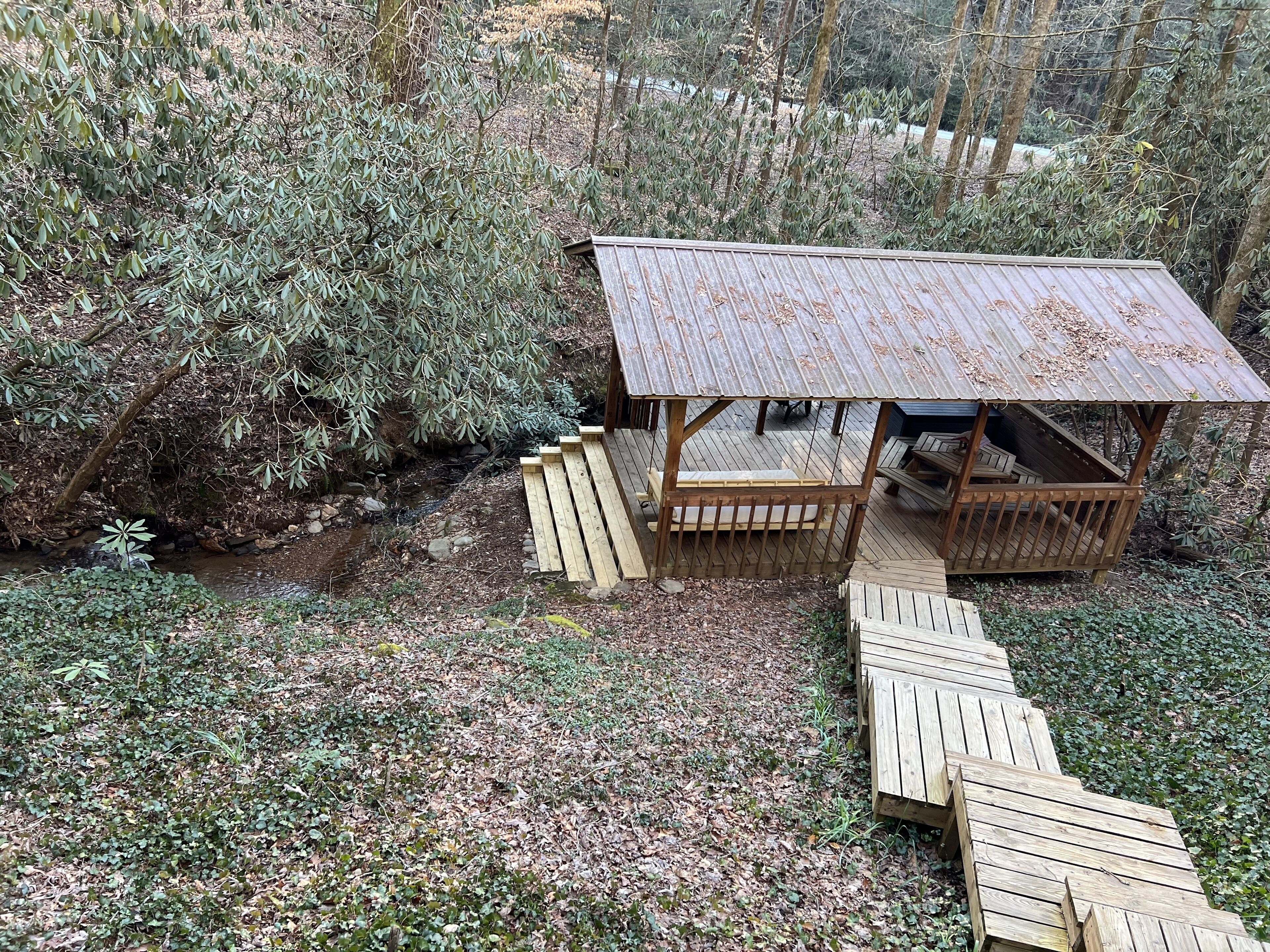 Une structure rustique en bois, surmontée d’un toit en métal, entourée d’une végétation luxuriante et accessible par une terrasse en bois.