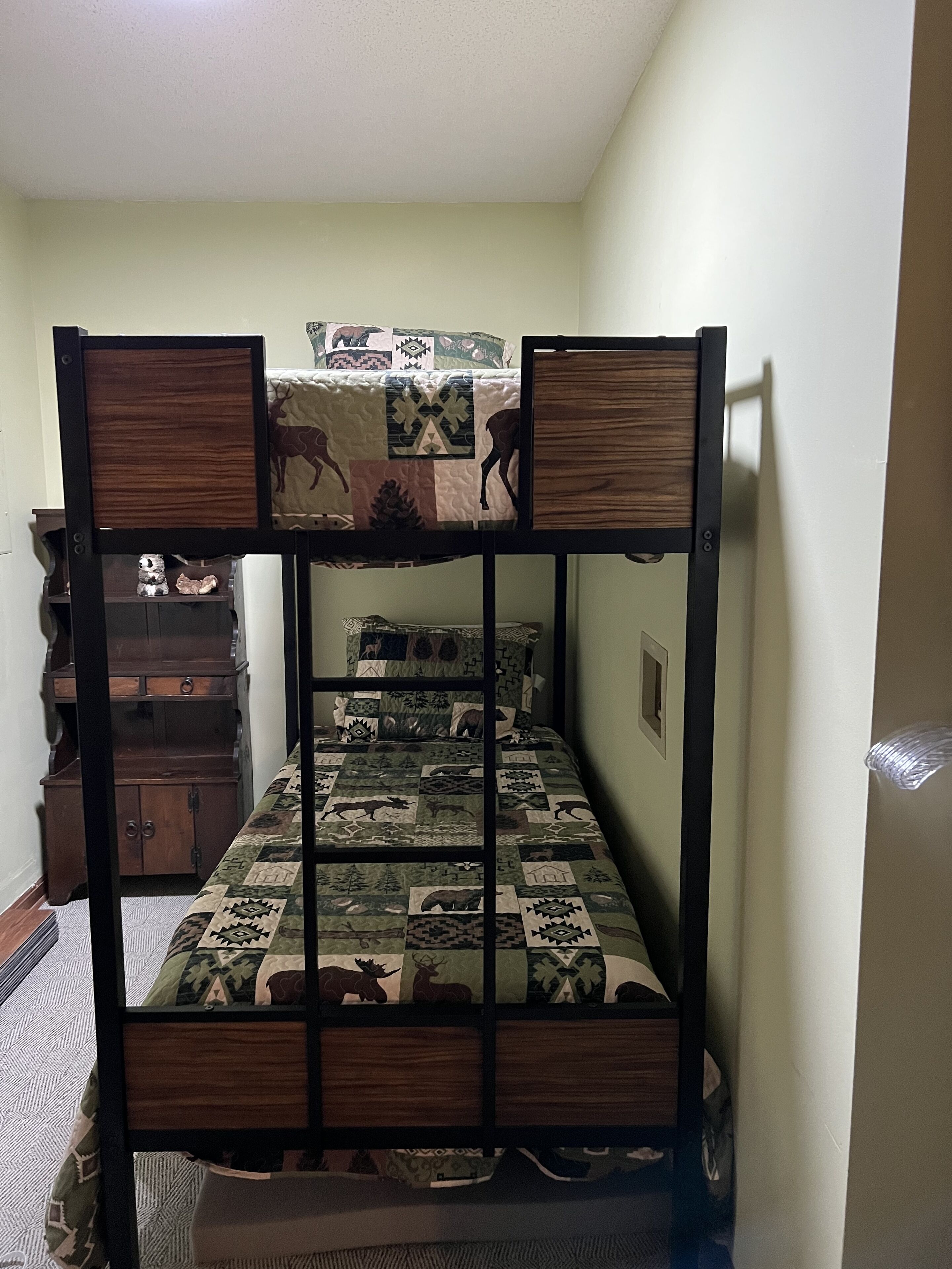 A bunk bed with a quilted mattress featuring animal prints, a wooden headboard, and a dresser with multiple drawers.