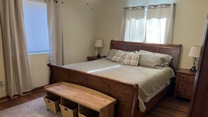 Une chambre à coucher avec un lit en bois, des tables de chevet, un banc et des paniers de rangement.