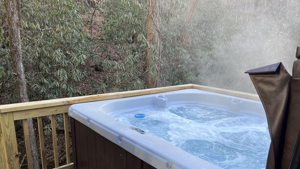Un bain à remous doté d’une terrasse en bois et d’un banc, entouré d’arbres.