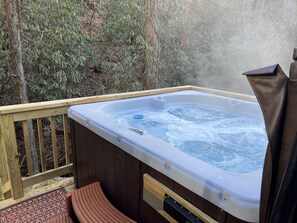 Ein Whirlpool mit Holzterrasse und Sitzbank, umgeben von Bäumen.