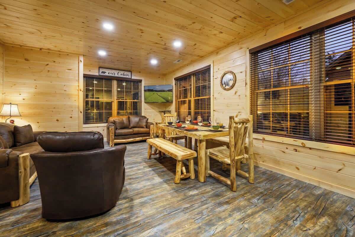 A wooden interior with a dining table, chairs, a sofa, and a television.