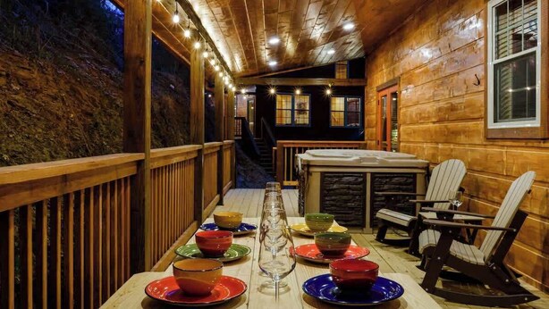 Interior de una cabaña de madera con una mesa de comedor para cuatro personas, una chimenea y sillas Adirondack.