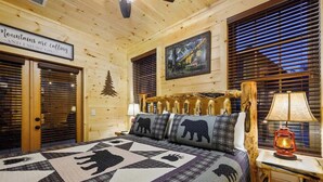 Interior de una cabaña de madera con una cama, un cartel que dice 'Mountains are calling' y un cuadro en la pared.