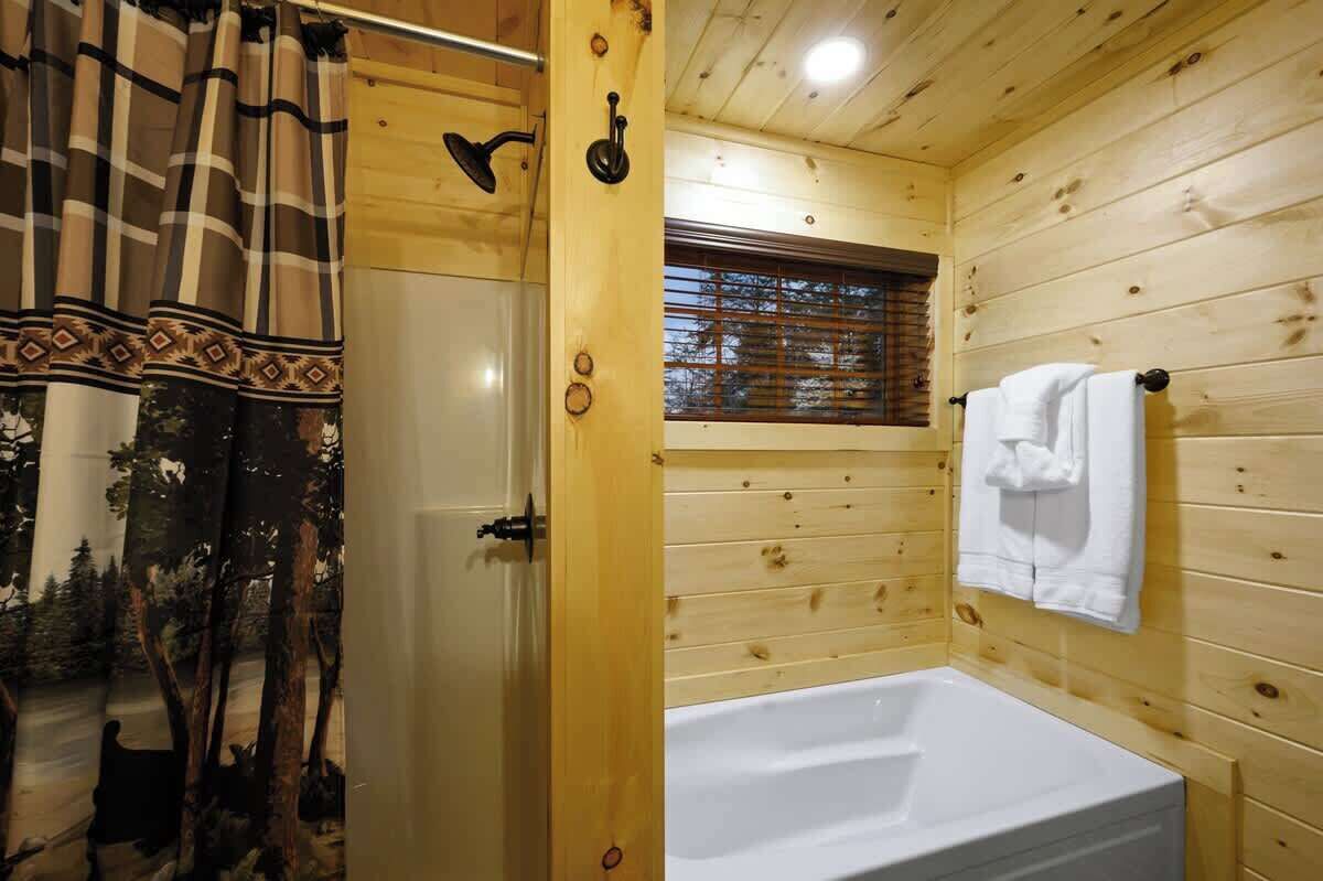 Une salle de bain rustique, avec des murs en bois, comprenant une baignoire, une fenêtre et un rideau de douche.