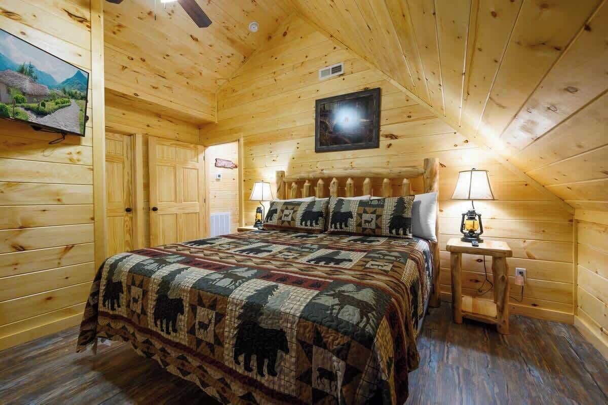 Une chambre à coucher dans un chalet en bois, avec une couvre-lit matelassé, un téléviseur fixé au mur et une table de chevet sur laquelle est posée une lanterne.