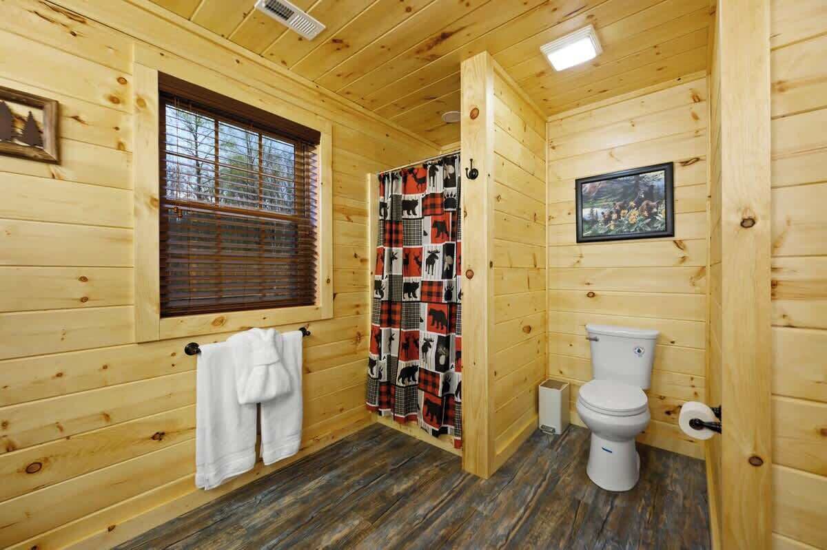 Ein Badezimmer einer Holzhütte mit Fenster, Duschvorhang, Toilette und Handtuchhalter.