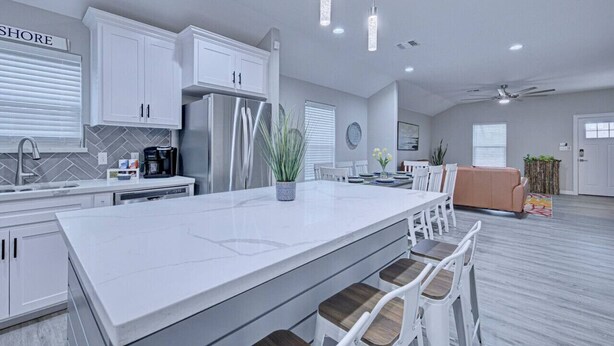 A modern kitchen with white cabinetry, a large island, and pendant lighting. - Howdy Holiday: Modern Family Getaway (Corpus Christi)