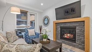 A living room with a fireplace, blue patterned sofa, and a coffee table. - Le Bucheron Stunning Spring Creek Luxury condo (Canmore)