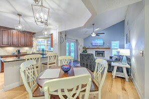 Une cuisine moderne avec des meubles en bois, un coin repas avec une table ronde et des chaises blanches, un ventilateur de plafond et un salon avec un canapé et un téléviseur.